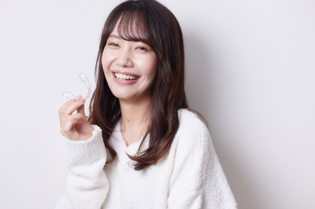 マウスピース矯正の装置を手に持って笑顔の女性